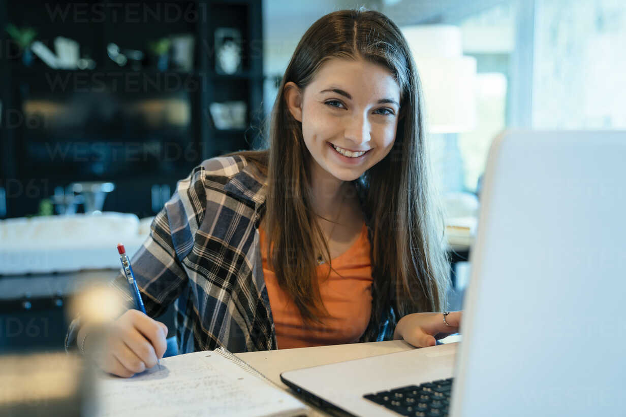 A young woman sitting at a laptop smiling at the camera. 