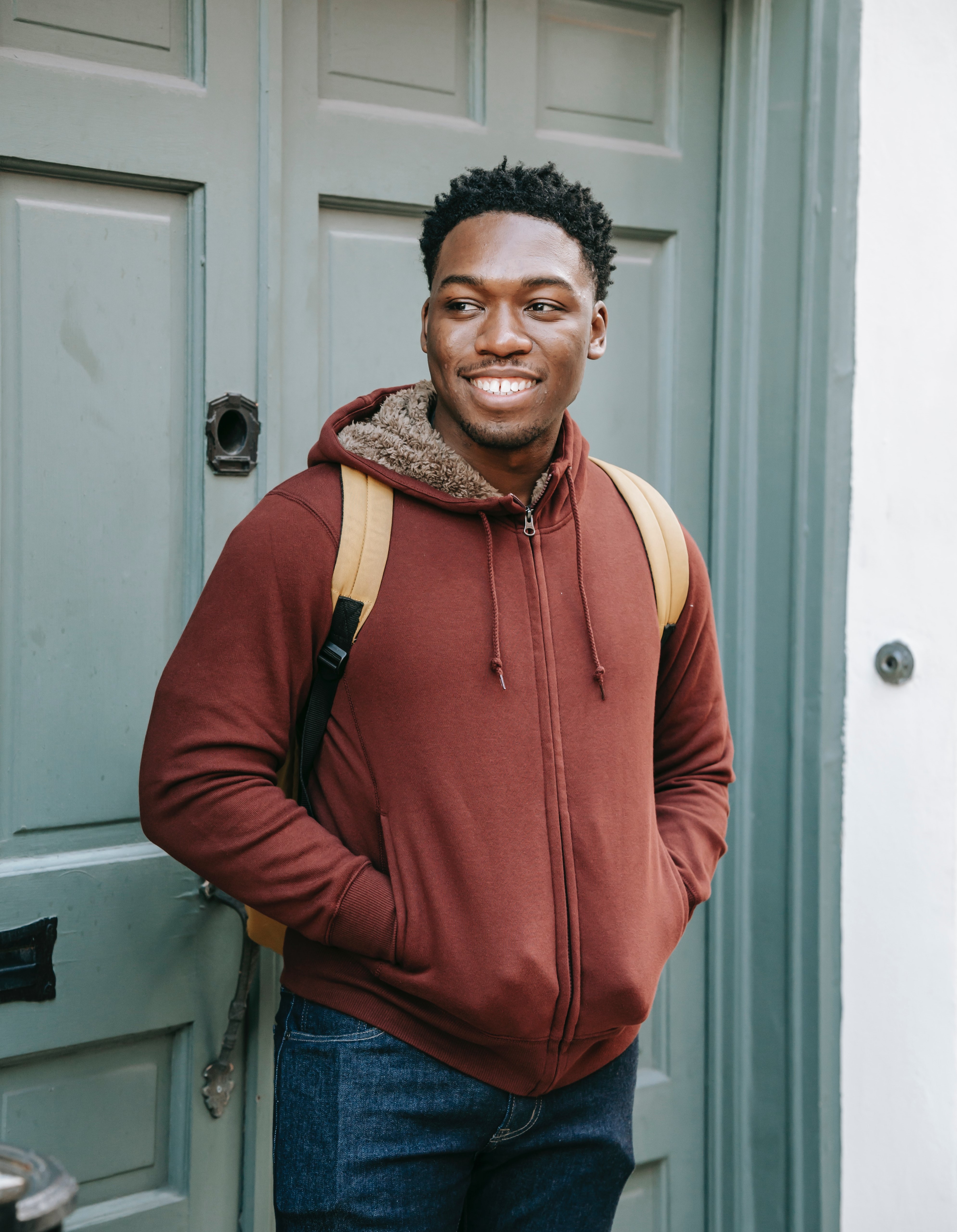 smiling young man stood in doorway wearing a back pack.