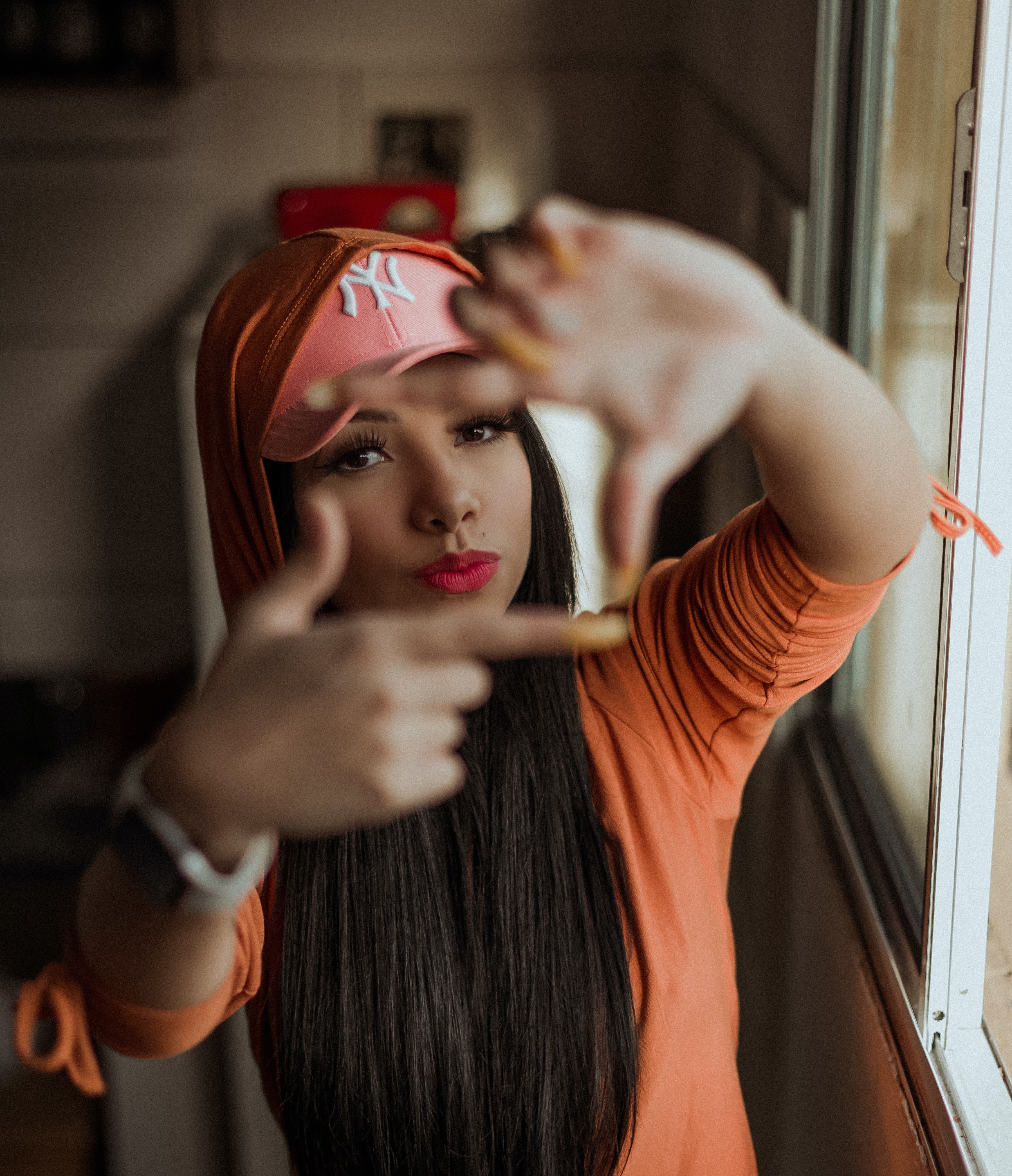 A young woman wearing a baseball cap holds her hands up in front of her face and uses her fingers to make a square frame.